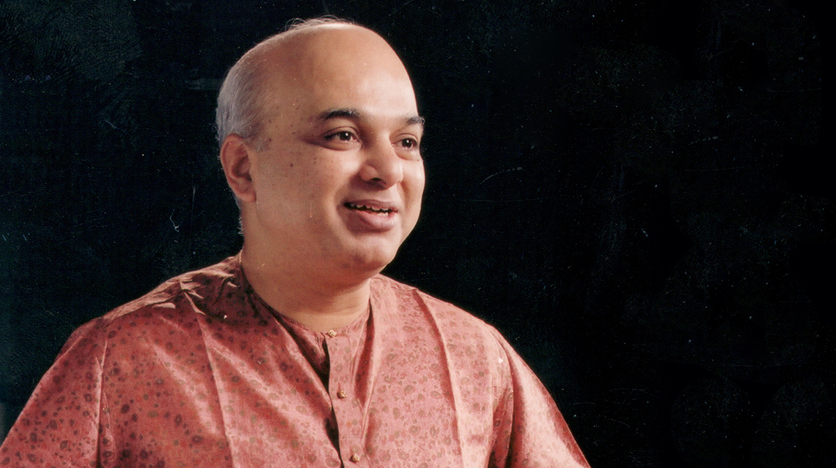A portrait of Pandit Satish Vyas, smiling against a black background.